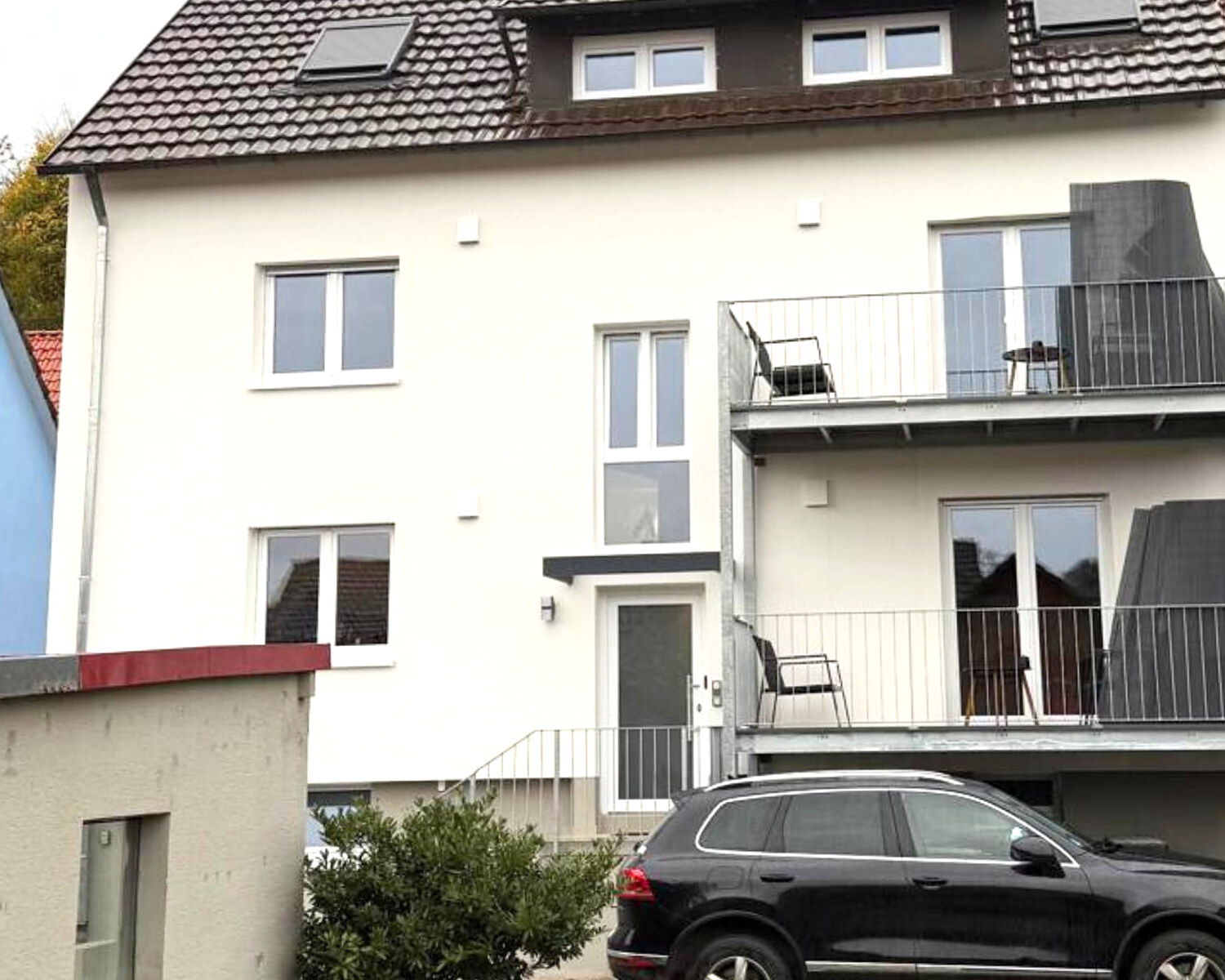 Dieselbe Gartenseite nach der Modernisierung: durchgehend helle Fassade, neue Fenster, verzinkte Stahl-Glas-Balkone
