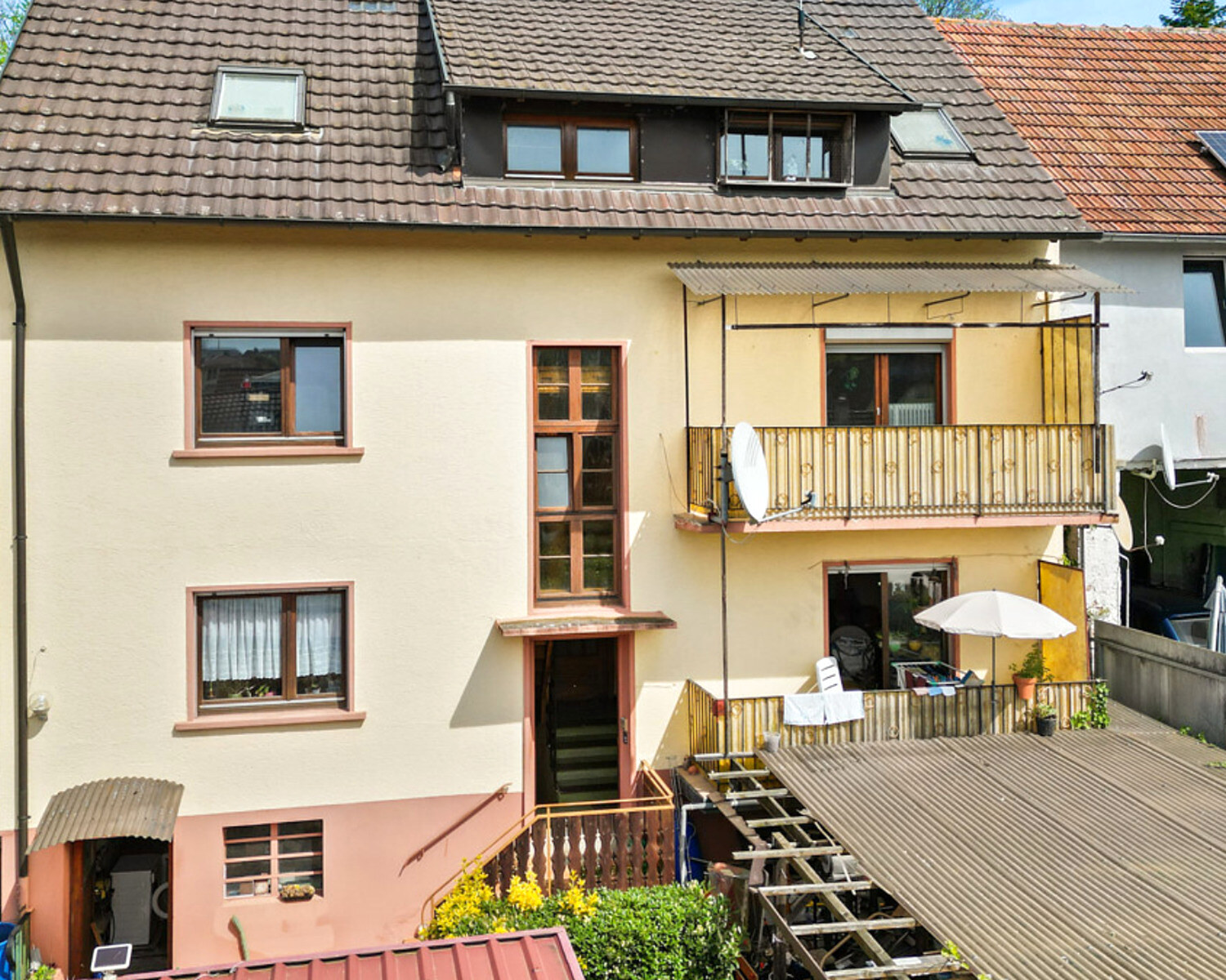 Gartenseite des Mehrfamilienhauses in Kippenheim vor der Modernisierung: alte Holzbalkone, Wellblech-Vordächer, abgesetzte Putzflächen